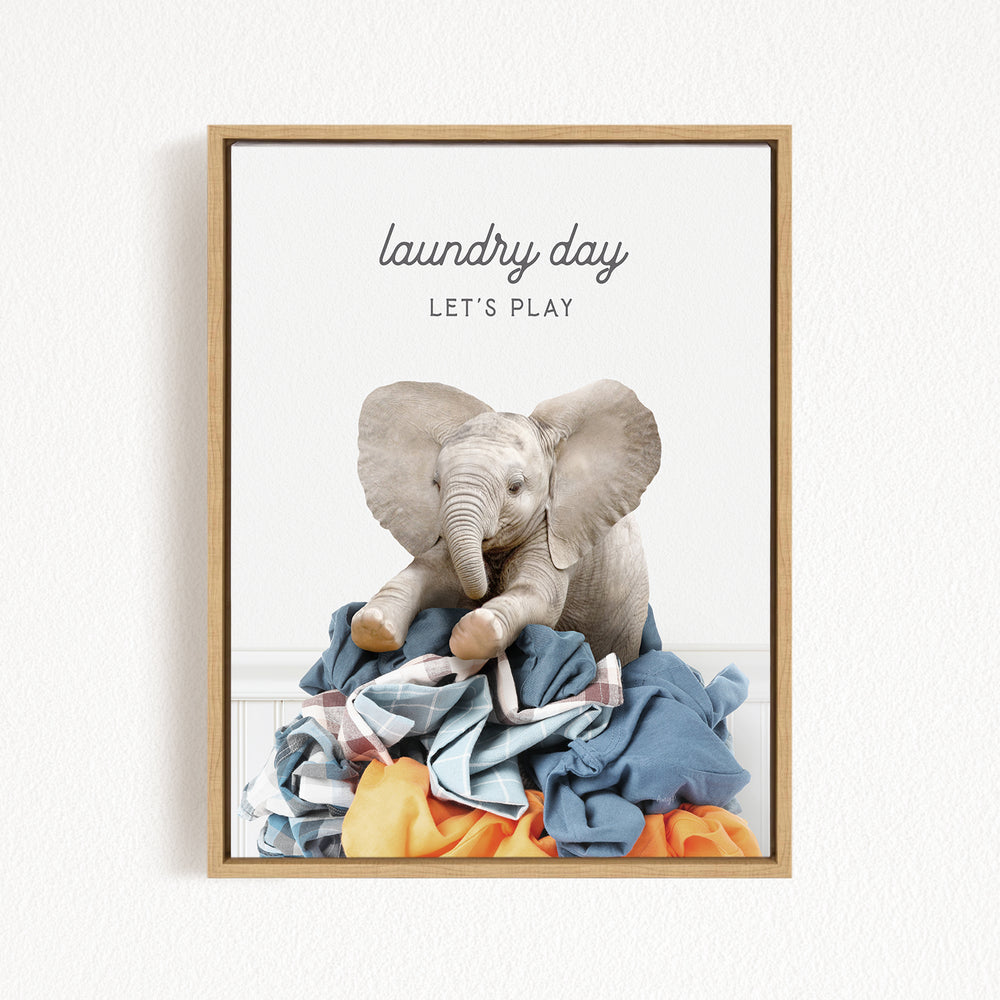 A framed image of a gray elephant sitting atop a pile of clothes, with the text "laundry day let's play" written above it.