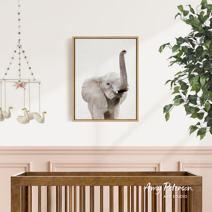a wooden crib with a framed picture of an elephant hanging on the wall above it.
