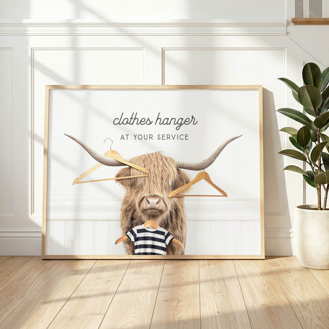 A large framed poster with a picture of a horned animal, possibly a yak or a yak dog, holding a pair of clothes hangers. The text on the poster reads "clothes hanger AT YOUR SERVICE".