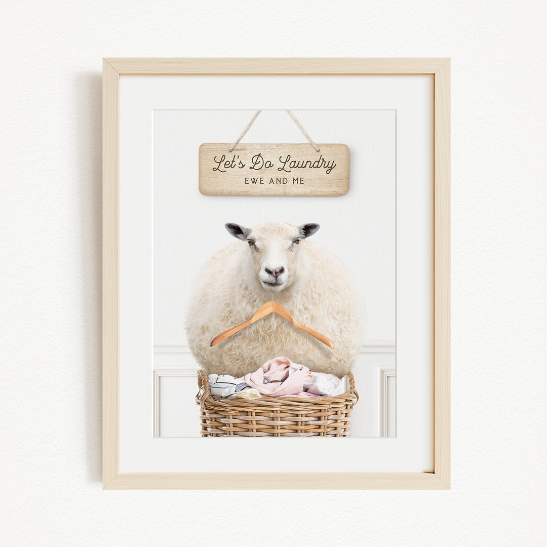 A framed image of a sheep sitting in a basket filled with laundry, with a sign above it that says "Let's Do Laundry Ew and Me".
