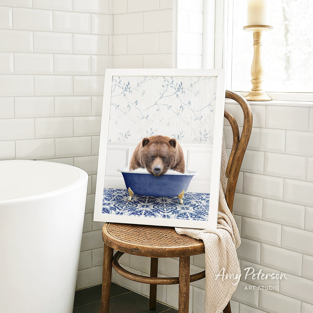 A framed image of a brown bear sitting in a blue bathtub, with a white tiled wall and a window in the background.