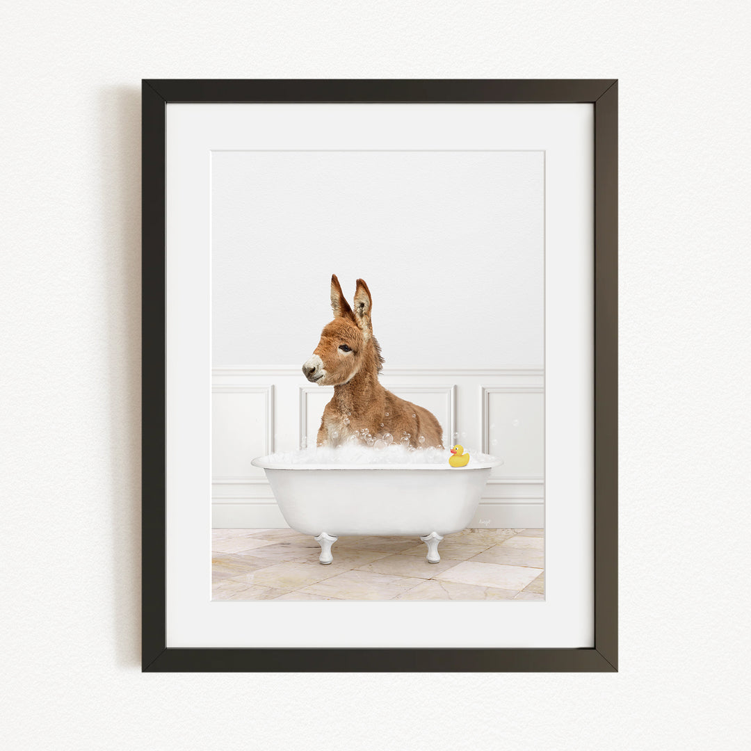 A donkey is sitting in a white bathtub filled with bubbles, with a yellow rubber duck floating in the water.