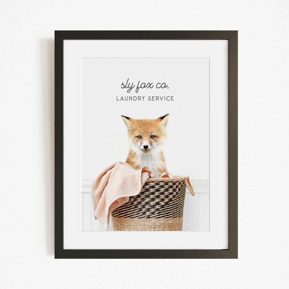 A framed image of a young fox sitting in a woven laundry basket, with the text "sky fox co. LAUNDRY SERVICE" displayed above the fox.