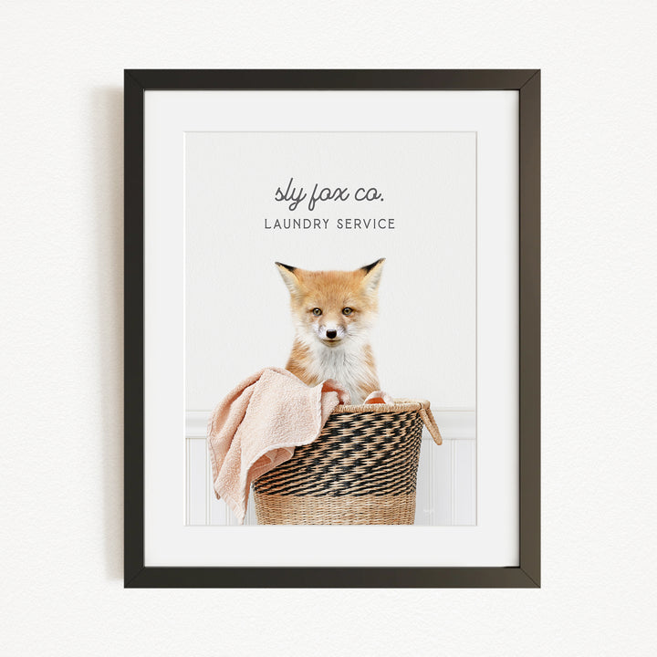 A framed image of a young fox sitting in a woven laundry basket, with the text "sky fox co. LAUNDRY SERVICE" displayed above the fox.