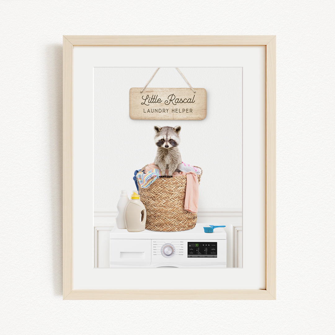 A framed image of a raccoon sitting in a laundry basket, with a sign above that says "Little Racquel Laundry Helper".