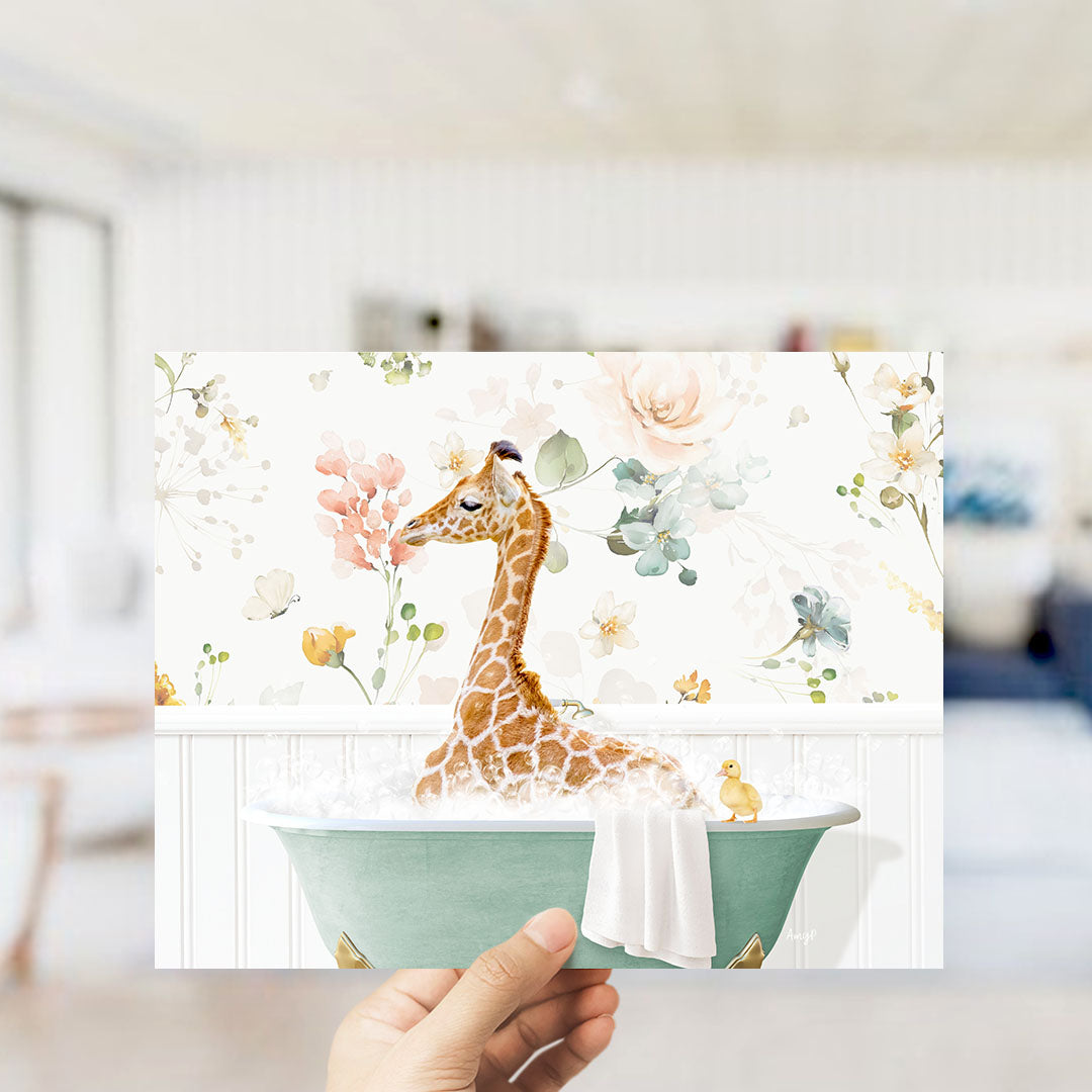 A hand holding a framed print featuring a giraffe sitting in a bathtub filled with water and surrounded by flowers.