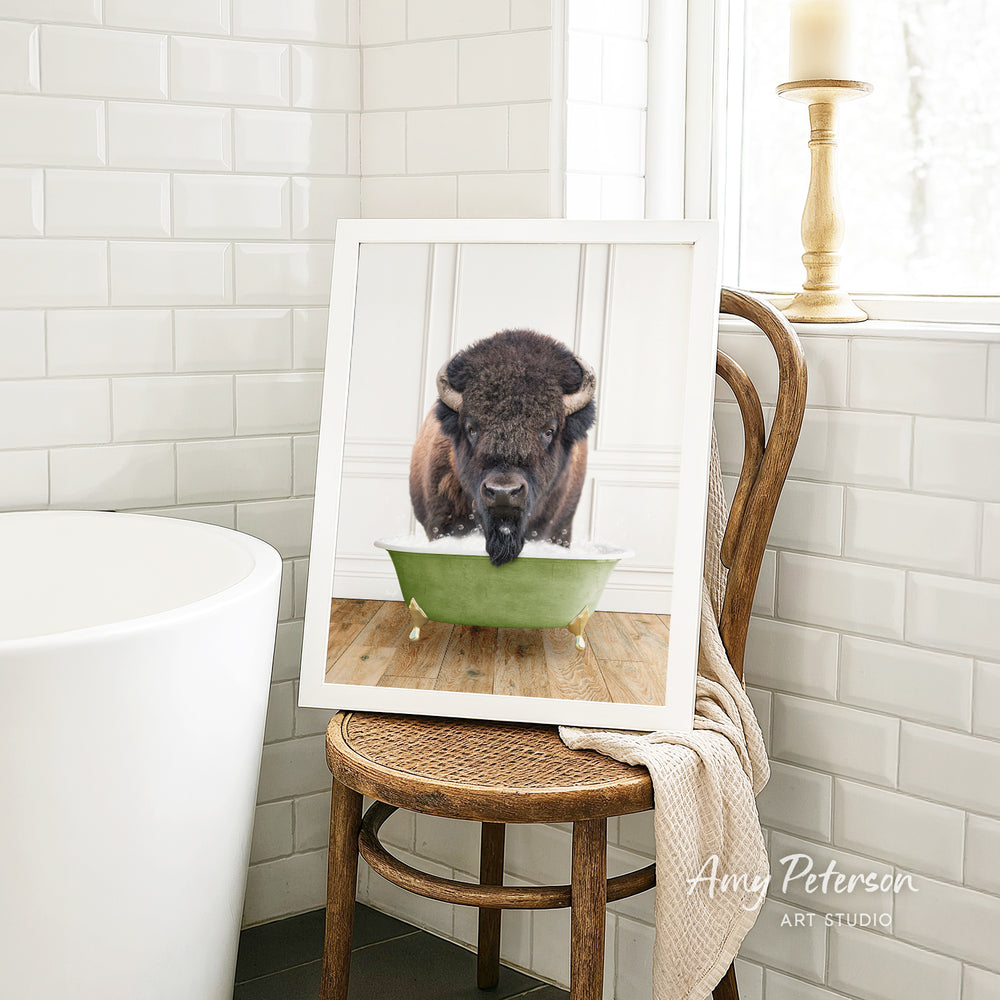A framed image of a bison sitting in a green bathtub, with a towel draped over the back of the chair.