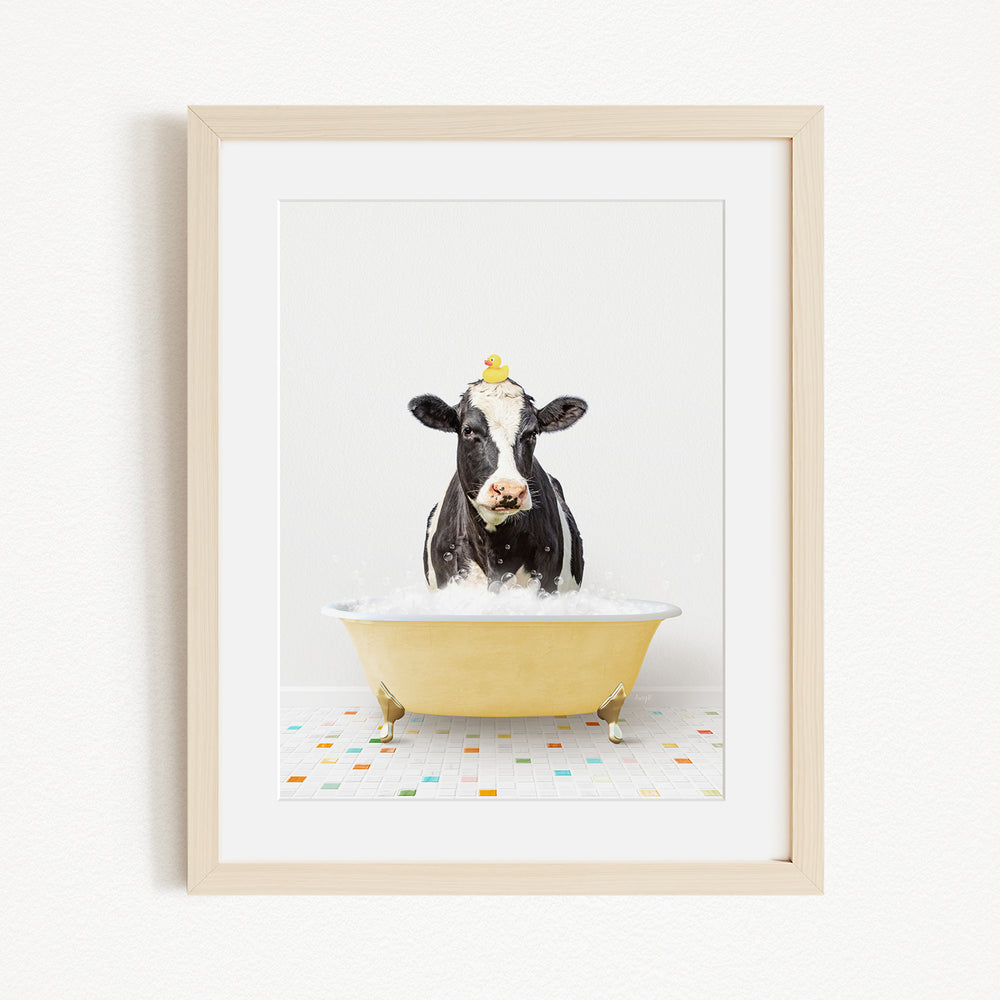 A black and white cow is sitting in a yellow bathtub filled with water, with a yellow rubber duck perched on its head.
