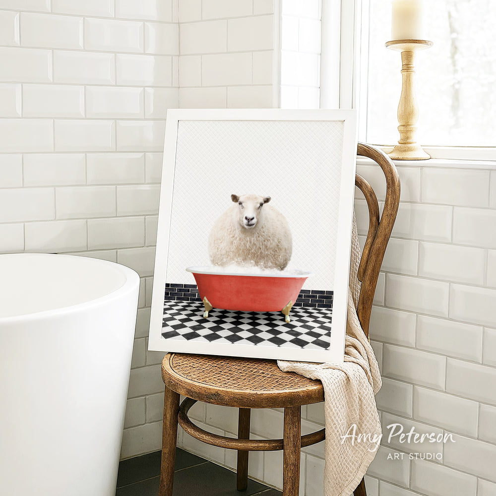 A framed image of a sheep sitting in a red bathtub, surrounded by a black and white checkered floor, is displayed on a wooden chair in a bathroom setting.