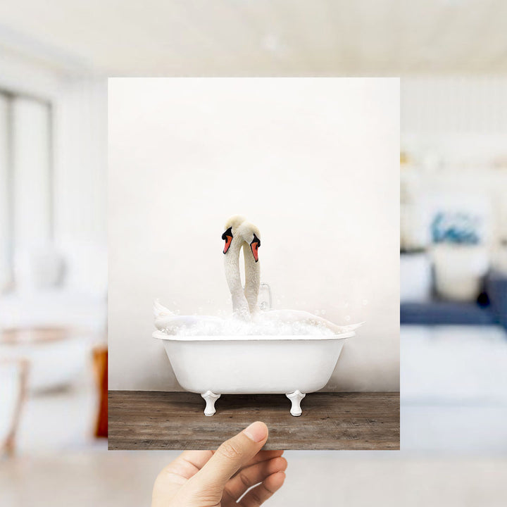 A hand holds up a photograph of two swans in a bathtub, with the swans appearing to be in mid-air.