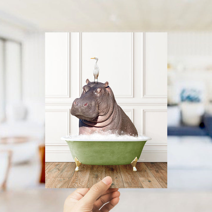 A hand holds up a photograph of a hippopotamus sitting in a bathtub, with a seagull perched on its head.