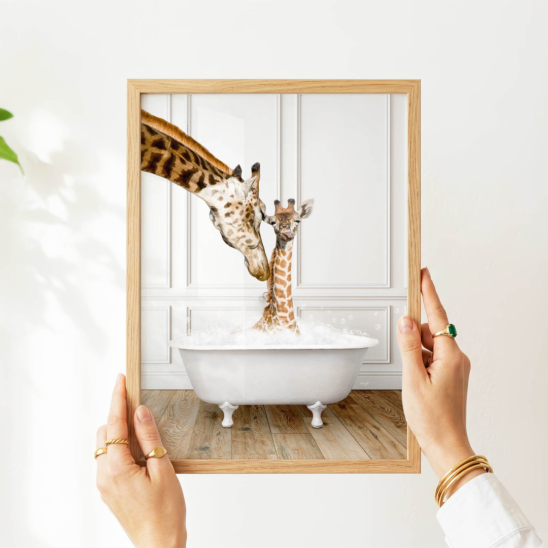 A person's hands holding a framed image of two giraffes in a bathtub, with one giraffe appearing to be a baby giraffe.