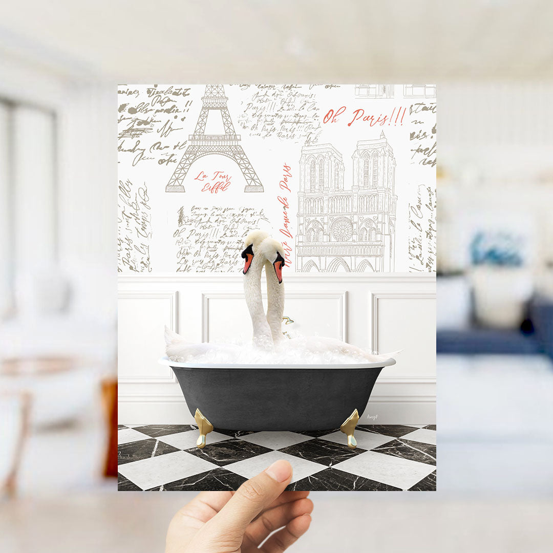 A hand is holding up a printed image featuring a swan sitting in a bathtub filled with bubbles, with the Eiffel Tower and Notre-Dame Cathedral visible in the background.