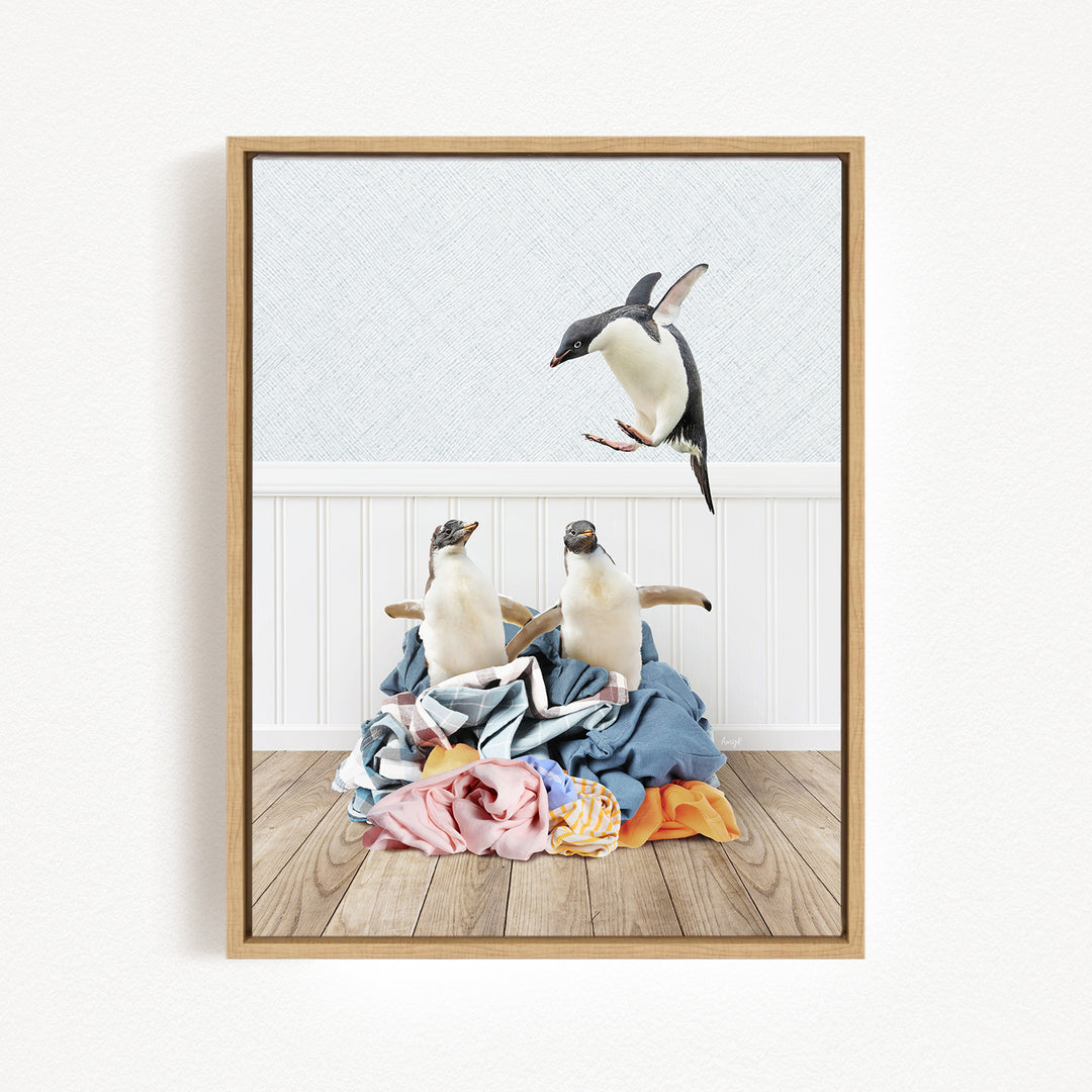 A framed image depicting two penguins standing on a pile of clothes, with one penguin flying towards the other.