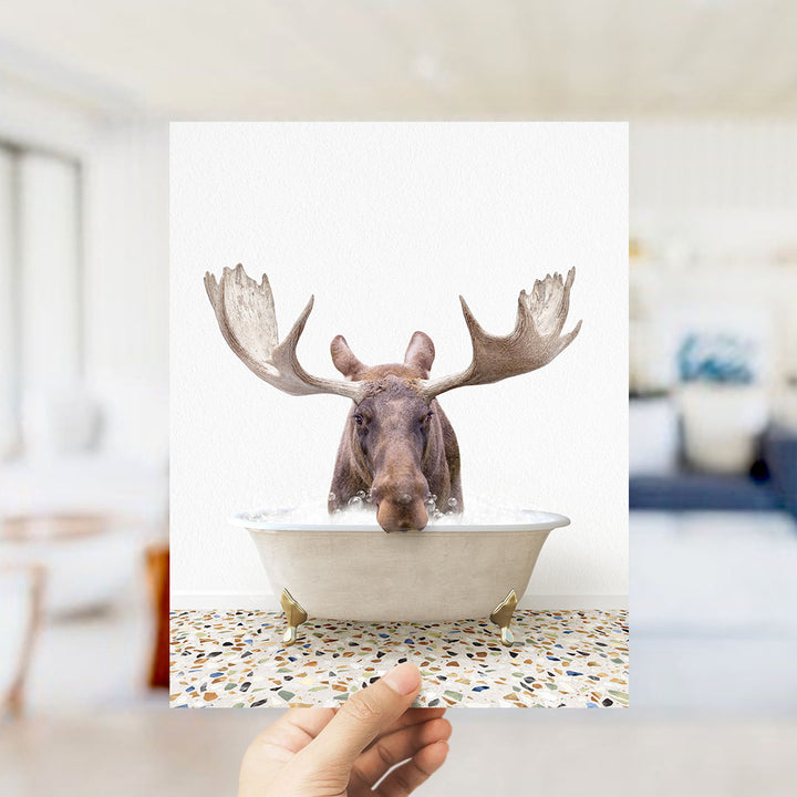 A moose with large antlers is sitting in a bathtub filled with water, creating a whimsical and humorous scene.