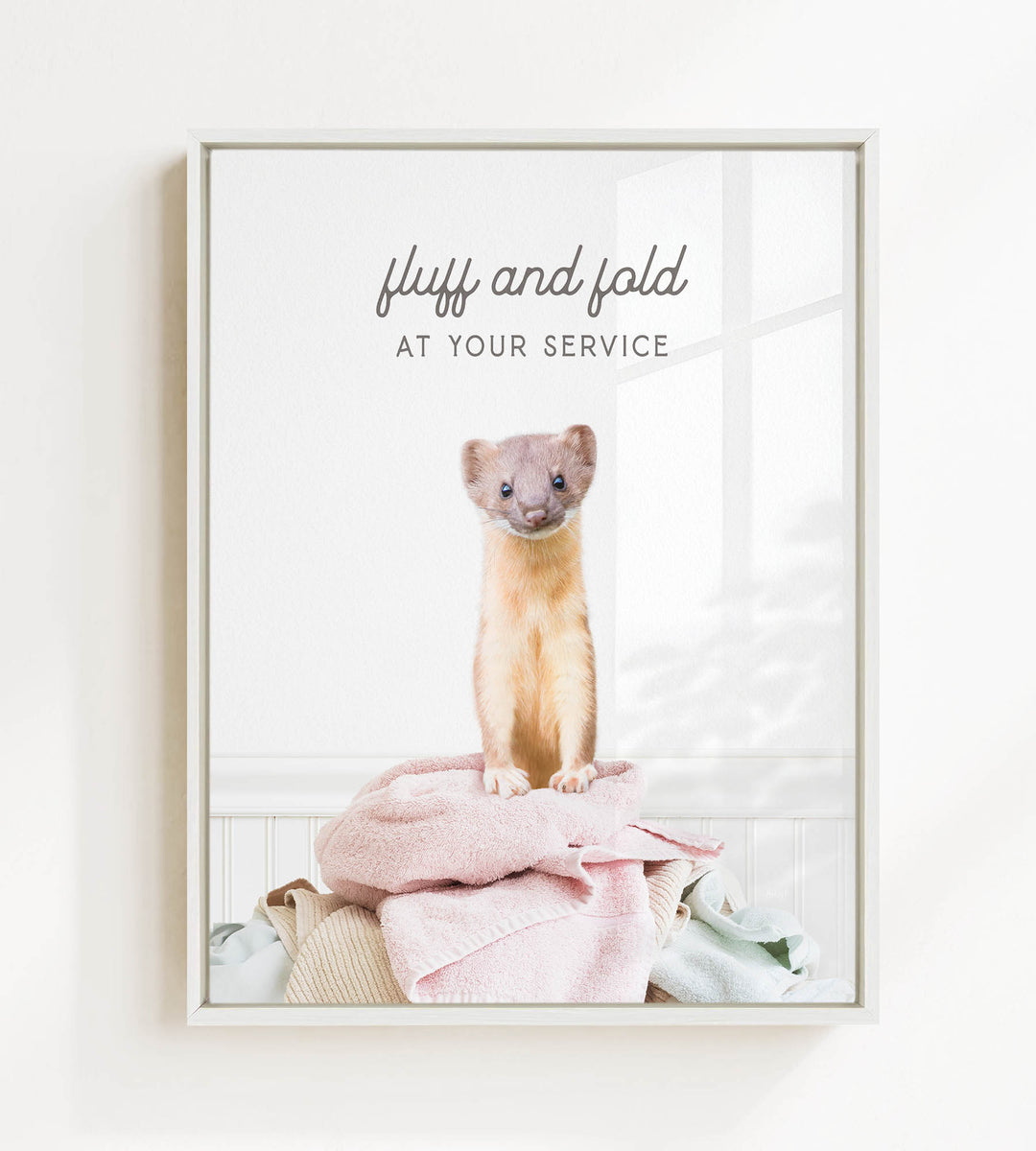 A small brown and white ferret standing on a pile of clothes, with the text "fluff and fold at your service" written above the image.
