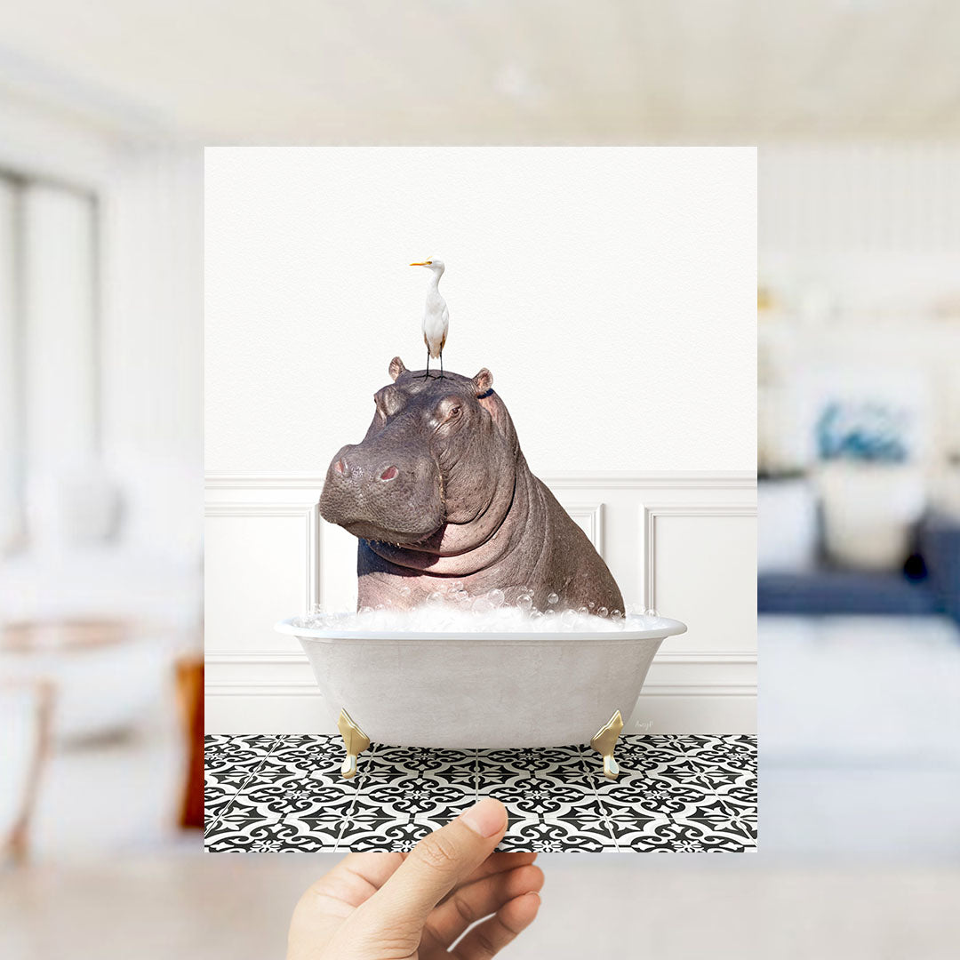 A hand holds up a framed image of a hippopotamus sitting in a bathtub, with a seagull perched on its head.