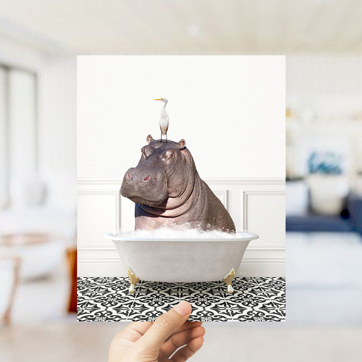 A hand holds up a framed image of a hippopotamus sitting in a bathtub, with a seagull perched on its head.