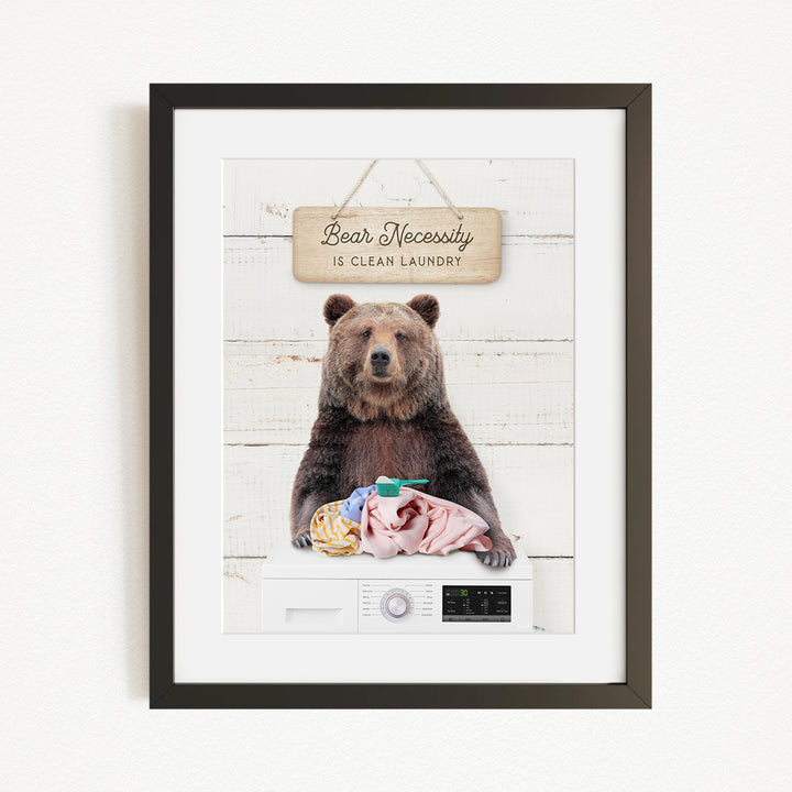 A framed image of a brown bear sitting on a washing machine, with a sign above it that says "Bear Necessity is clean laundry".