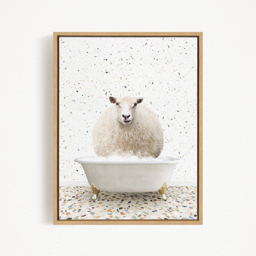 A fluffy white sheep is sitting in a white bathtub filled with bubbles, surrounded by a speckled tiled floor.