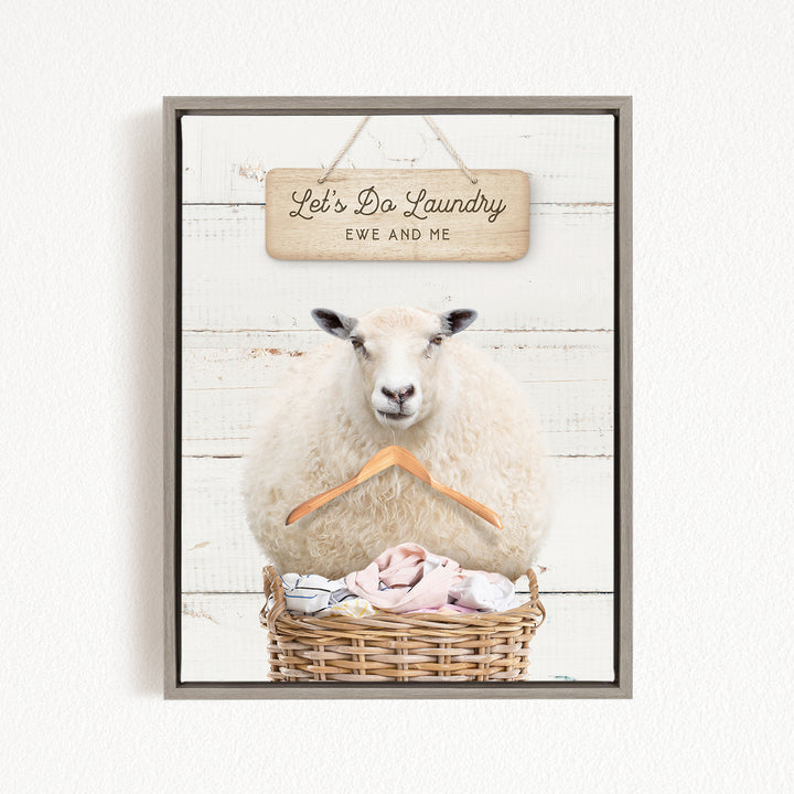 A framed image of a sheep sitting in a basket filled with laundry, with a sign above that says "Let's Da Laundry Ewe and Me".