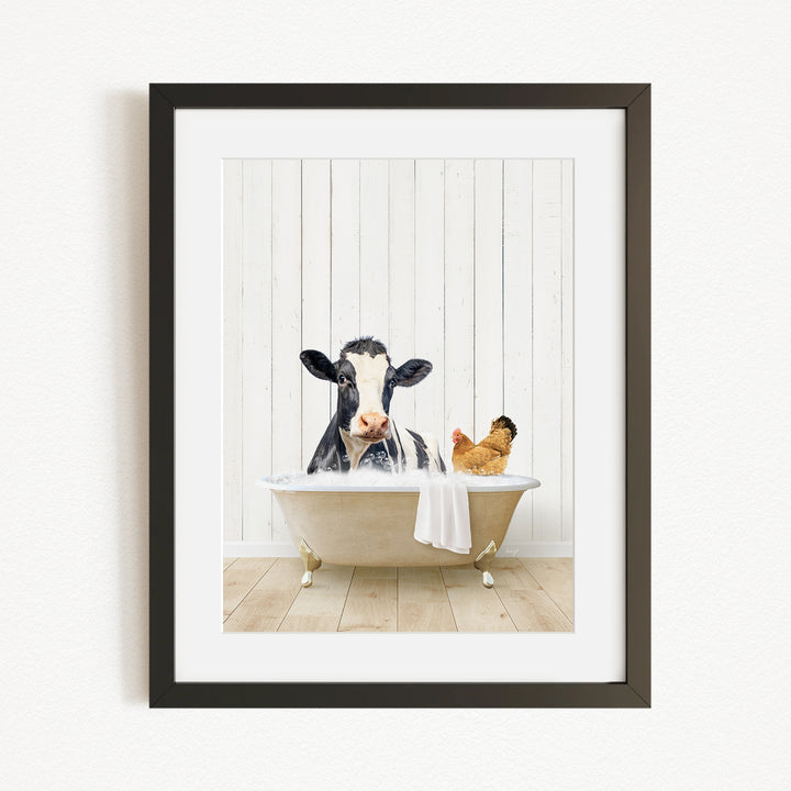 A black and white cow is sitting in a bathtub, with a chicken standing nearby, in a white wooden wall.