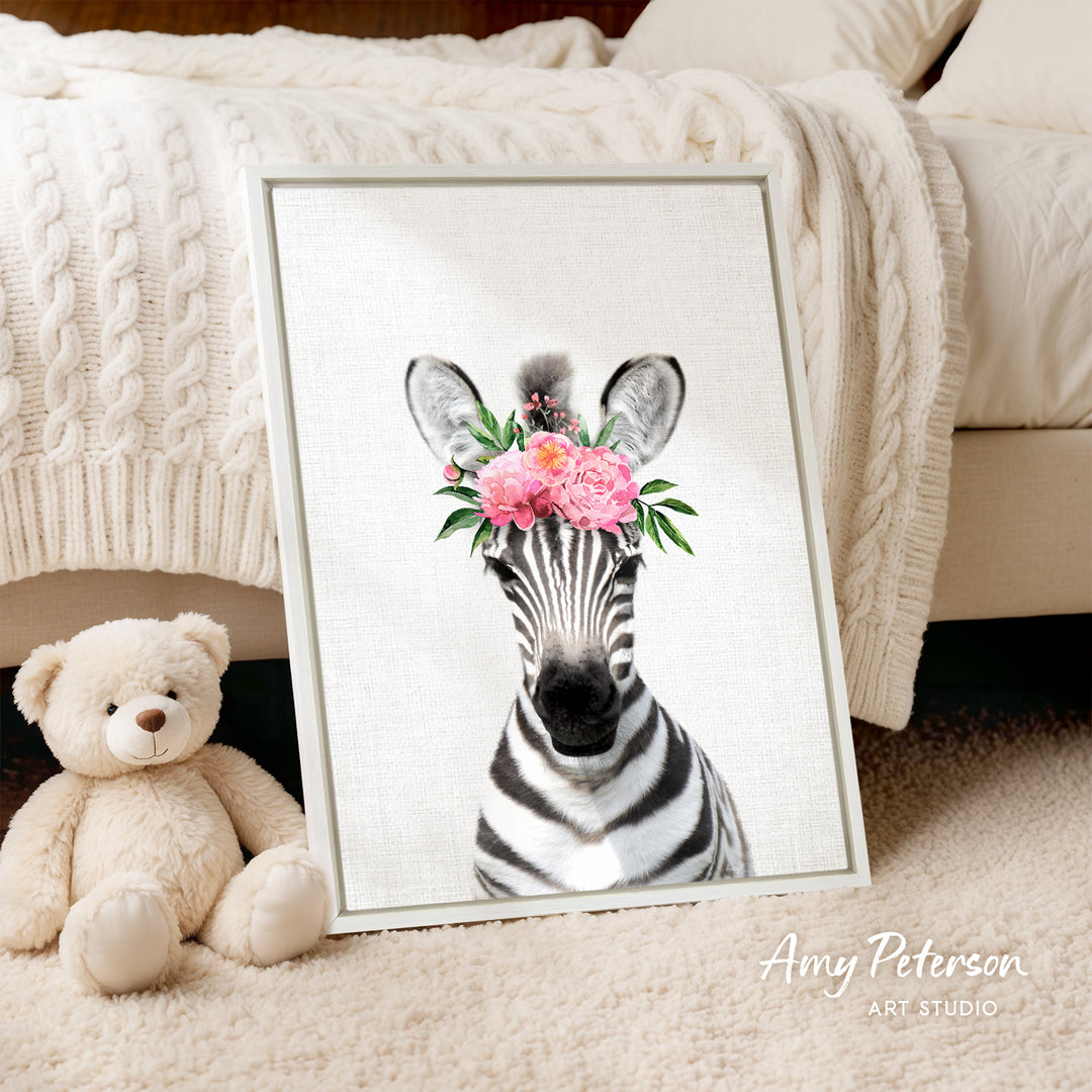 A framed print of a zebra wearing a floral headpiece is displayed on a beige carpet, accompanied by a teddy bear.