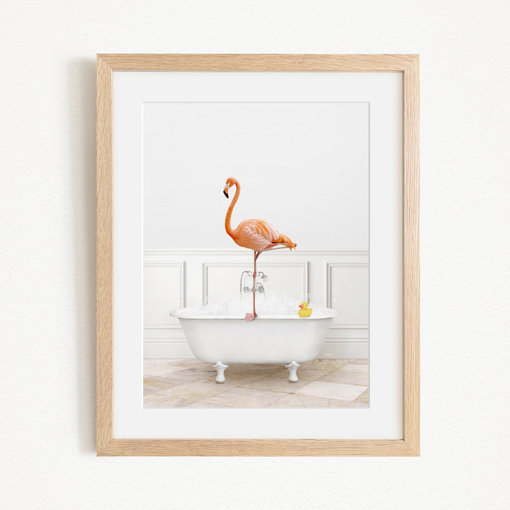 A framed image of a flamingo standing on one leg in a white bathtub filled with water and a yellow rubber duck.