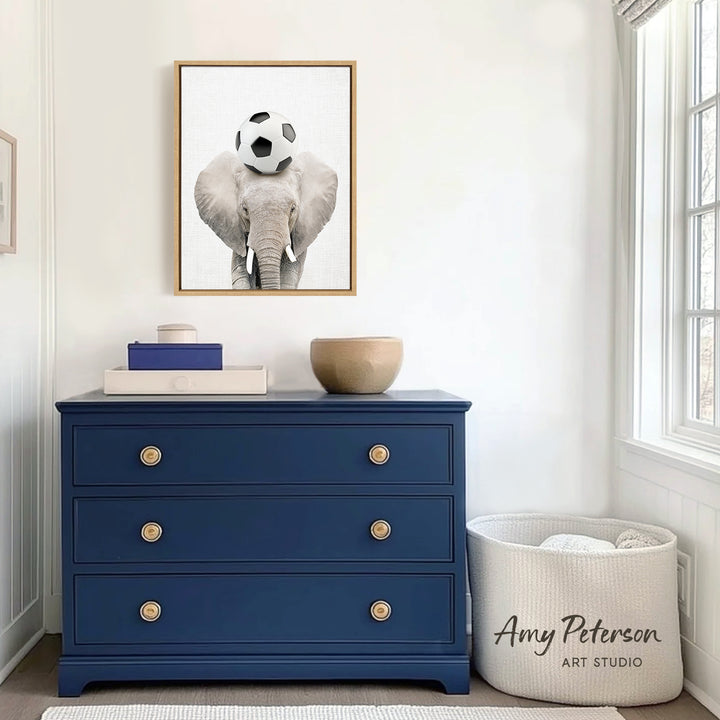 a blue dresser with a framed picture of an elephant holding a soccer ball on its head, placed above it. The dresser has three drawers and a white basket with the text " Amy Peterson ART STUDIO" on it.