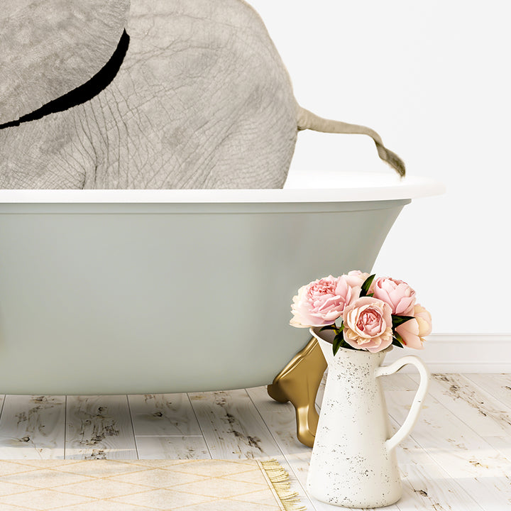 A white porcelain vase filled with pink flowers sits on a wooden floor next to a green bathtub, with a gray elephant partially visible in the background.