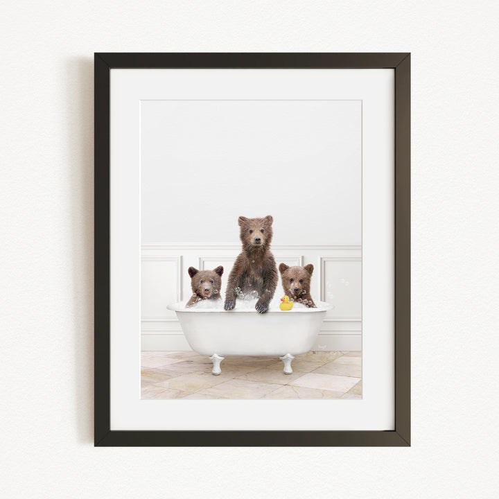 A framed image showing three brown bears sitting in a white bathtub, with one bear holding a yellow rubber duck.