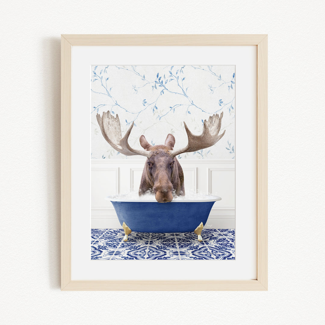 A moose with large antlers is sitting in a blue bathtub, surrounded by a blue and white patterned rug and a white wall with blue floral wallpaper.