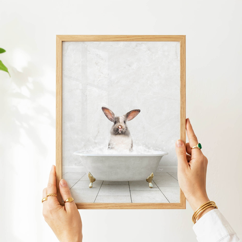 A person's hands are holding a framed picture of a rabbit sitting in a bathtub filled with water.