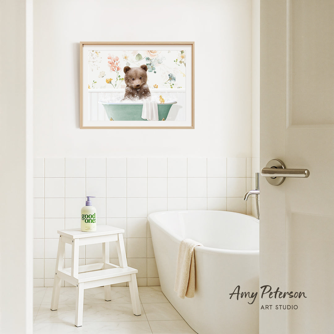A framed image of a bear sitting in a bathtub is hanging on a white tiled wall above a white bathtub in a bathroom.