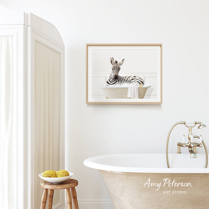a zebra sitting in a bathtub, with a framed picture of the zebra hanging on the wall above the bathtub.