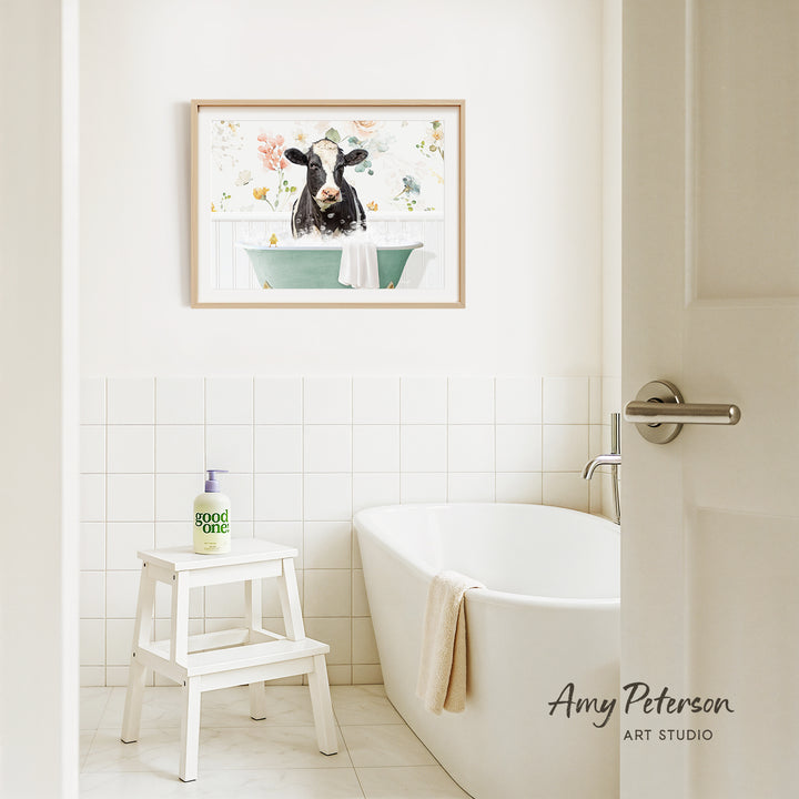 a bathroom with a white bathtub, a stool, and a framed picture of a cow in a bathtub hanging on the wall.