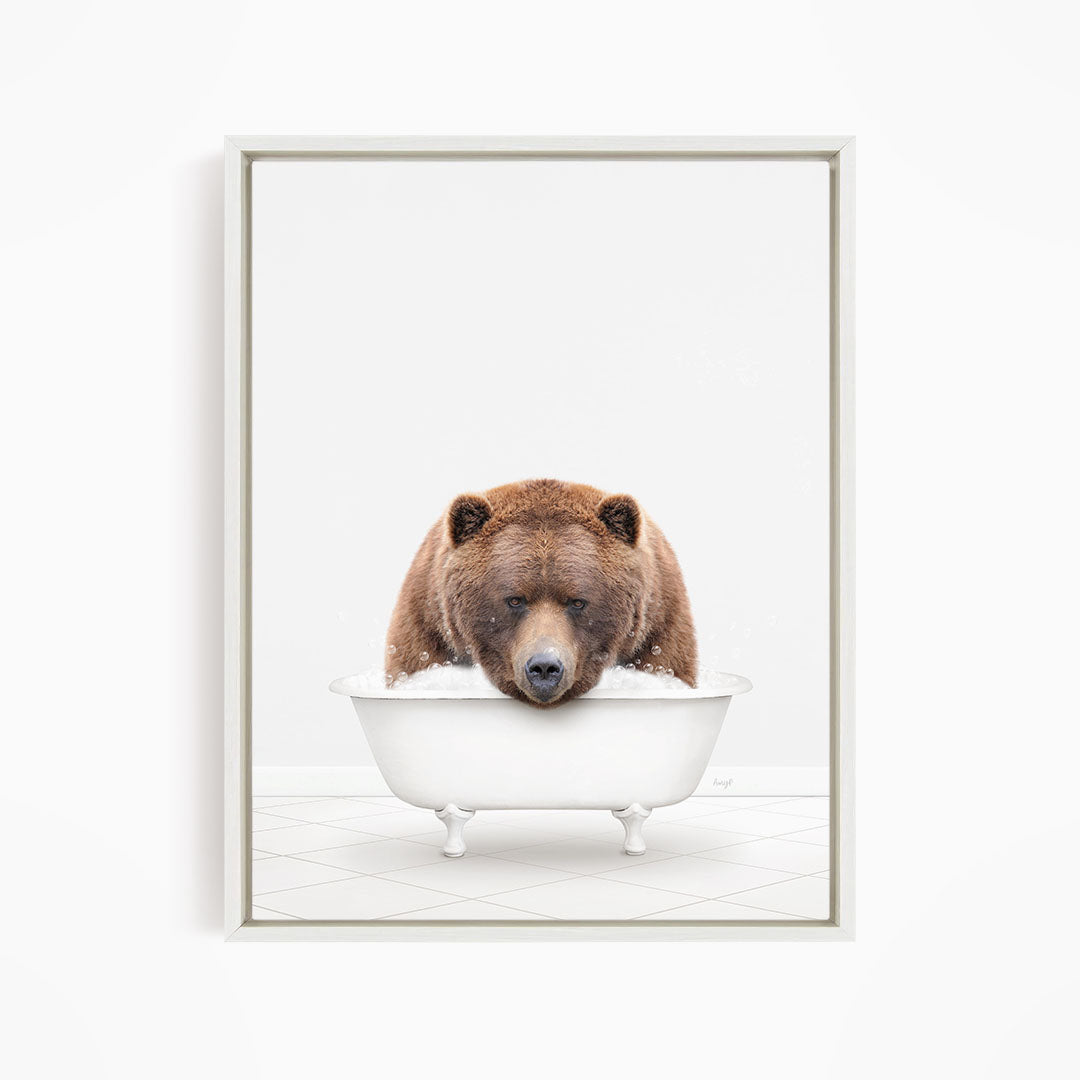 A brown bear is sitting in a white bathtub filled with water, appearing to enjoy the bath.