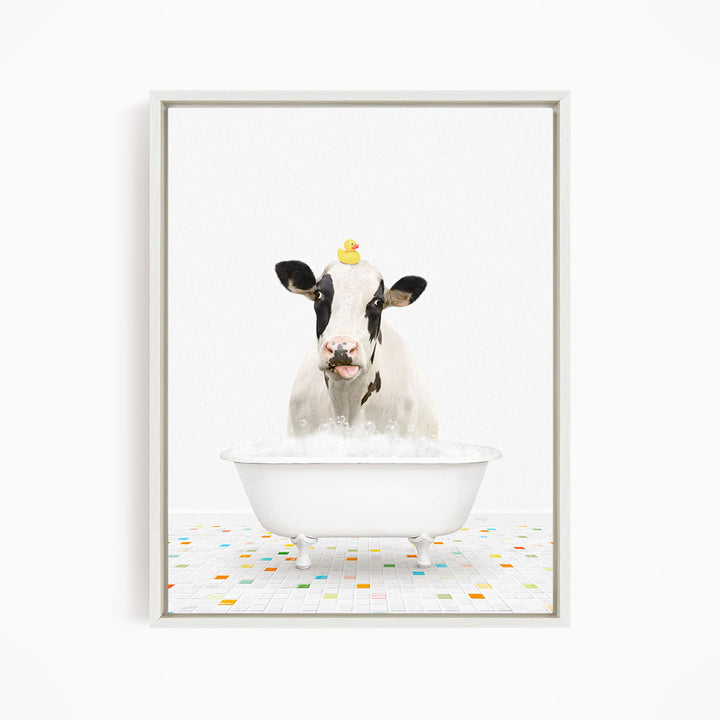 A black and white cow is sitting in a white bathtub filled with bubbles, with a yellow rubber duck perched on its head.