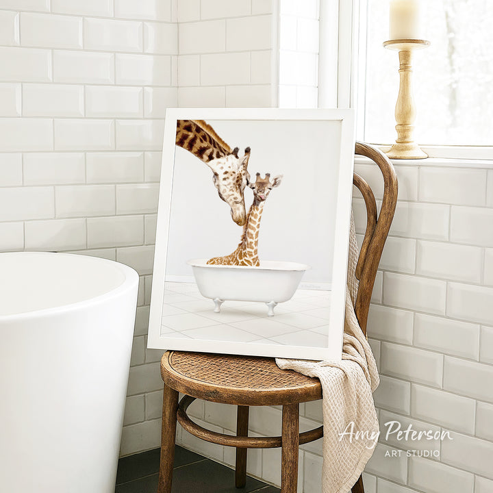 A framed photograph of two giraffes sitting in a bathtub, with one giraffe appearing to be feeding the other.