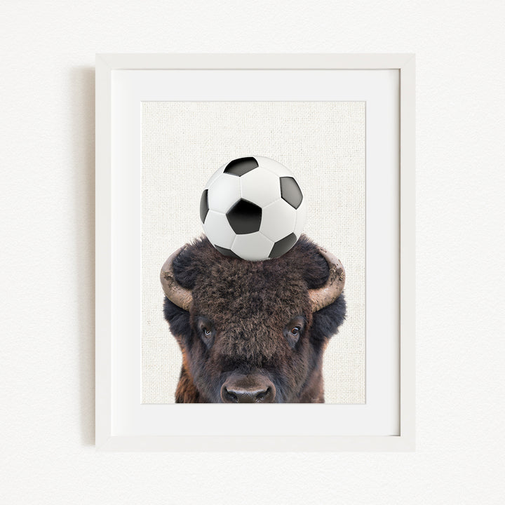 A framed image of a bison with a soccer ball on its head.