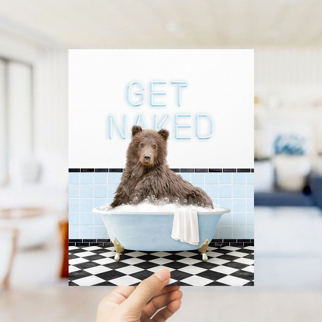 A hand holding a printed image of a brown bear sitting in a bathtub with the text "GET NAKED" displayed above it.