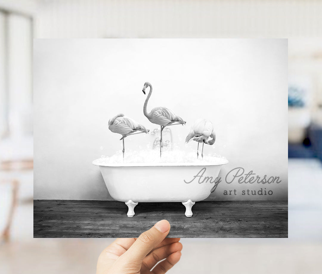 a person holding up a card with three flamingos in a bathtub