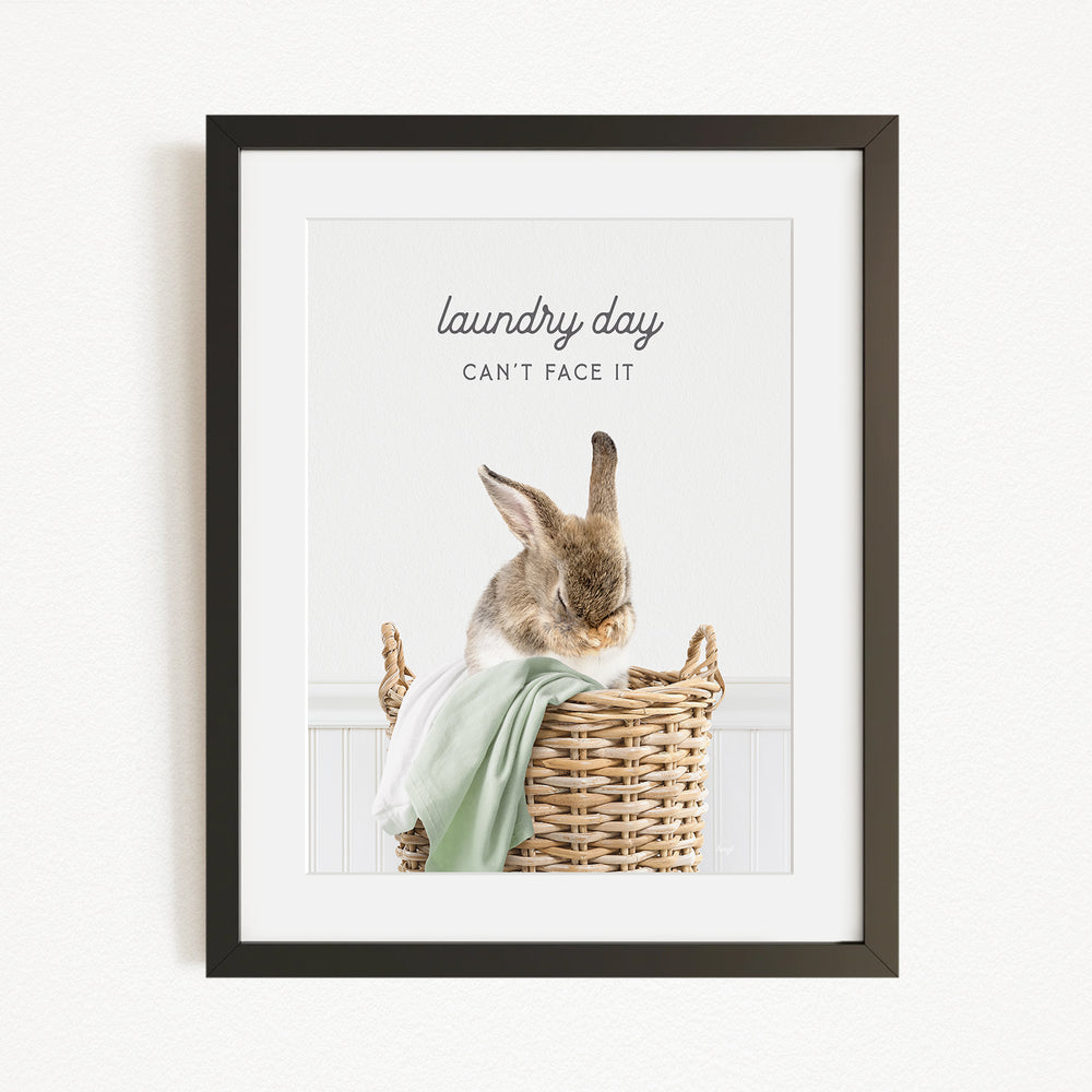 A framed image of a rabbit sitting in a wicker basket, with the text "laundry day can't face it" written above the rabbit.