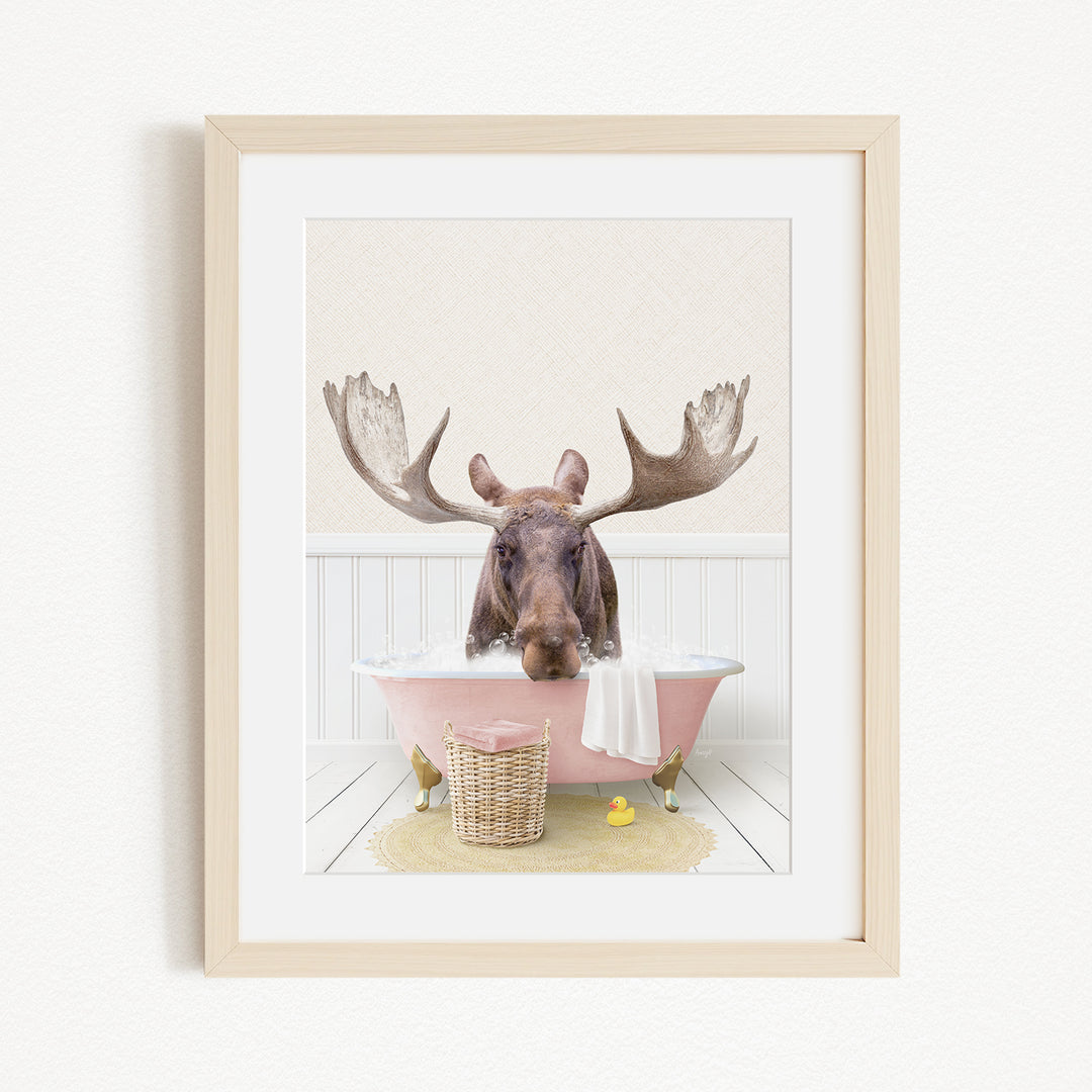 A moose with large antlers is sitting in a pink bathtub, surrounded by a yellow rubber duck and a basket.