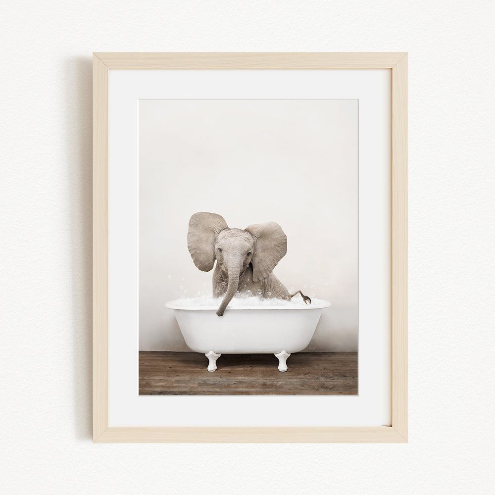 A baby elephant sitting in a white bathtub, with its trunk submerged in the water.