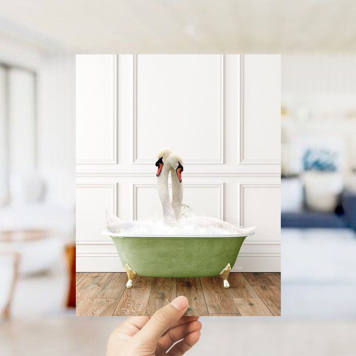 A hand holds up a photograph of a green bathtub filled with water, with two swans standing inside it.