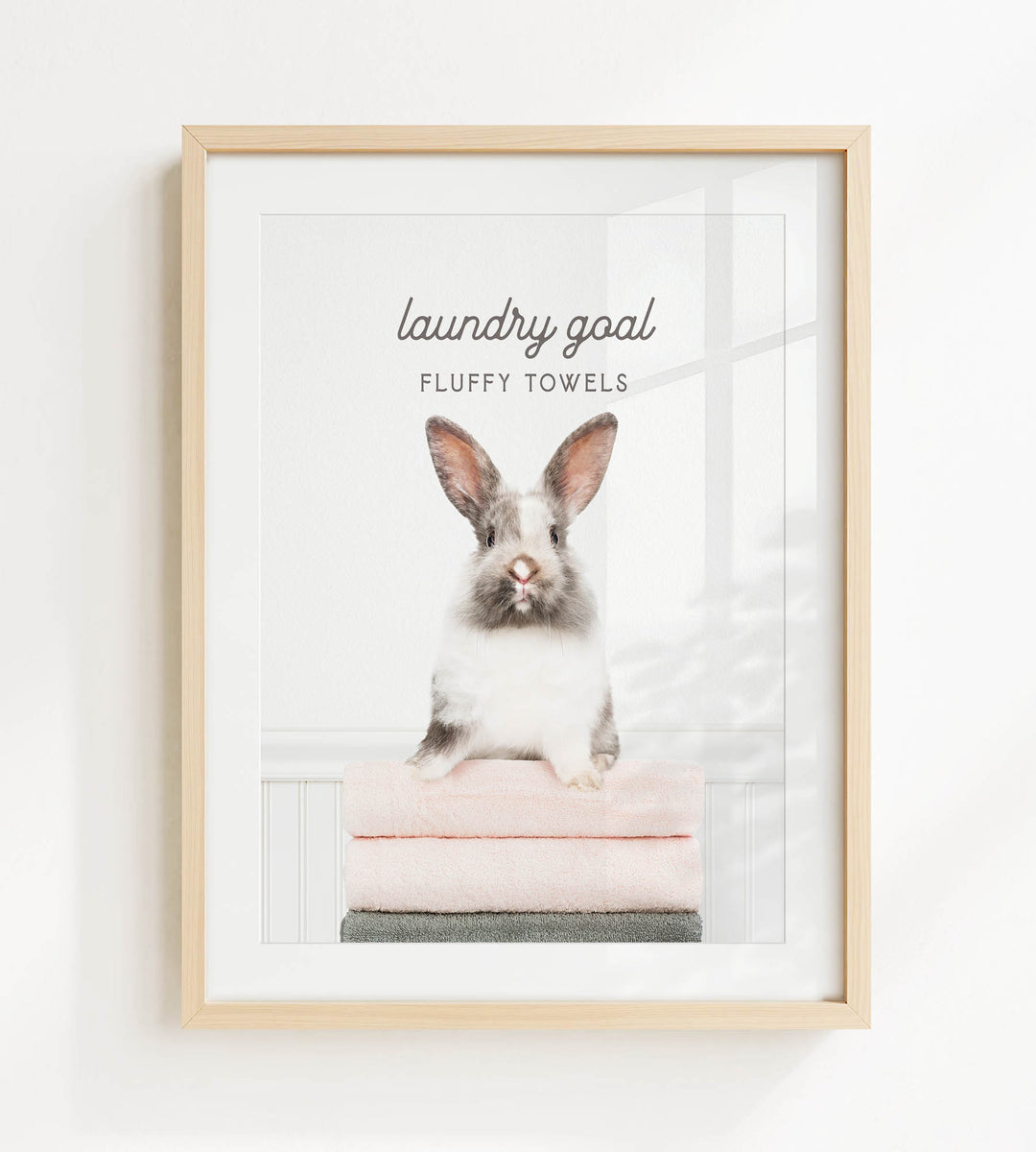 A framed image of a fluffy white rabbit sitting on a stack of pink towels, with the text "laundry goal" and "FLUFFY TOWELS" displayed above the rabbit.