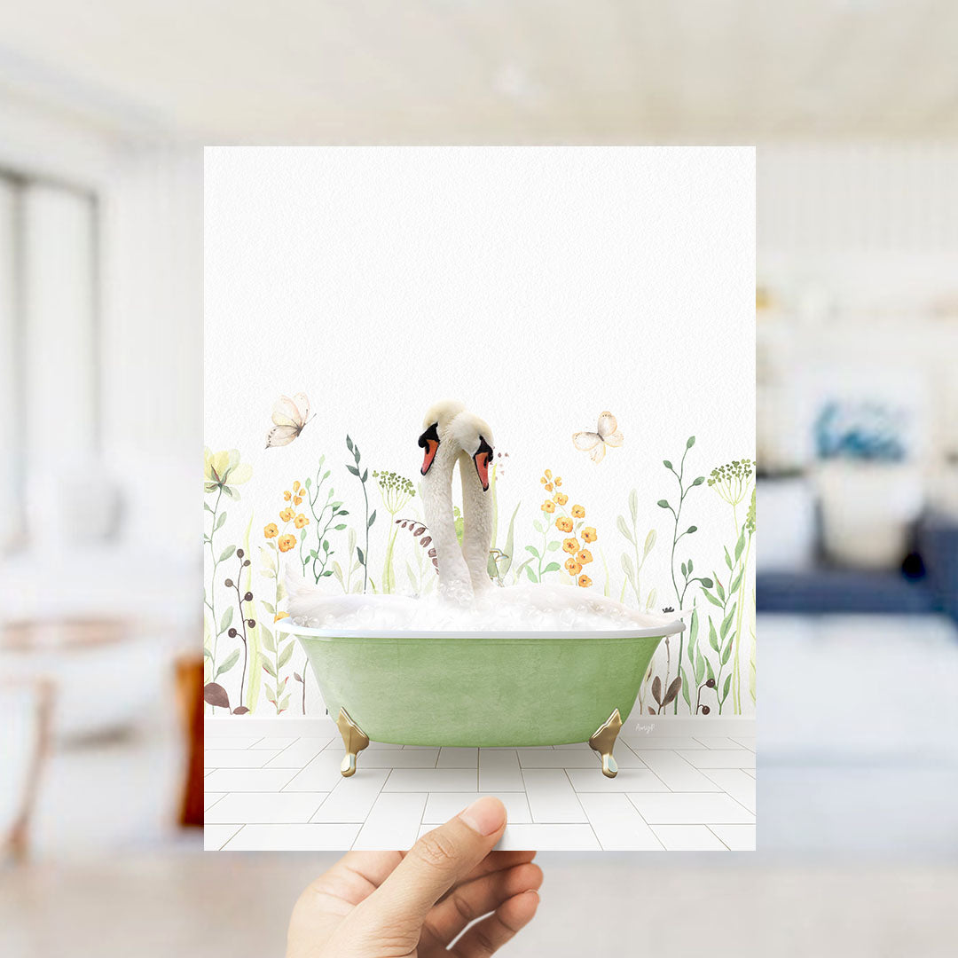 A hand holds up a framed image depicting a green bathtub filled with bubbles, with two swans sitting inside and surrounded by flowers and butterflies.