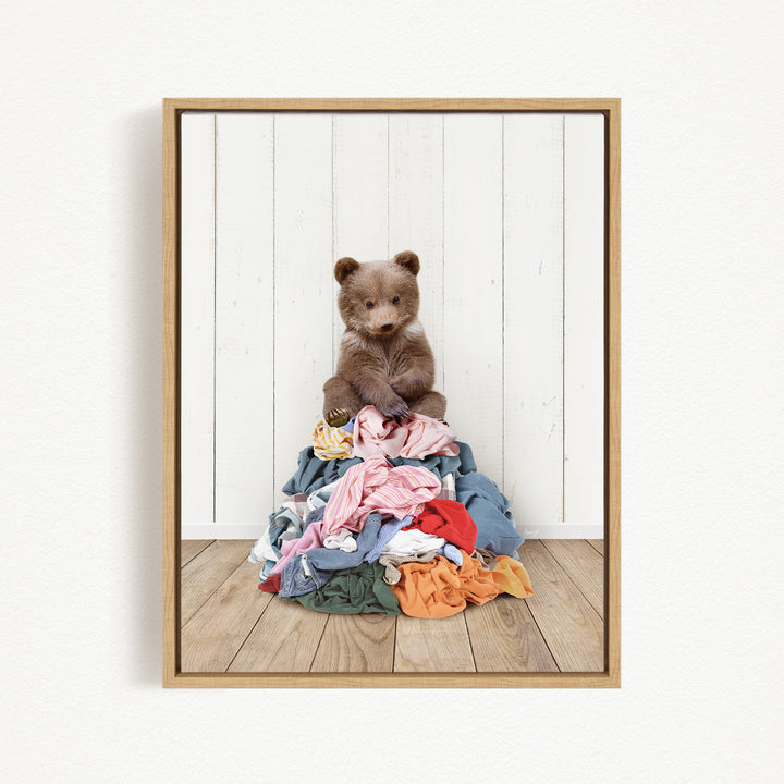 A teddy bear sitting atop a pile of clothes on a wooden floor.