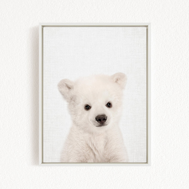 A cute white polar bear cub peering directly at the camera.